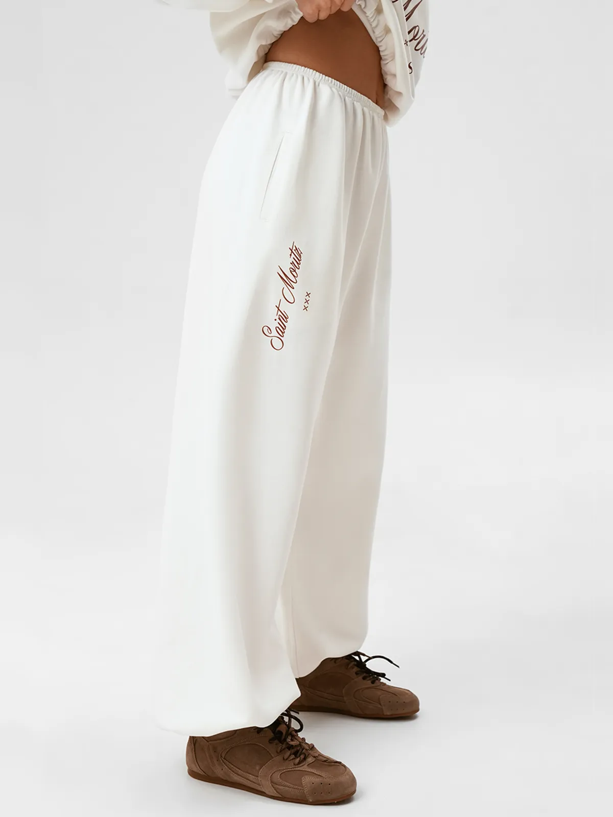 Модель в полный рост, одетая в молочные широкие брюки PANTS NEVE и свитшот, стоит на белом фоне.
