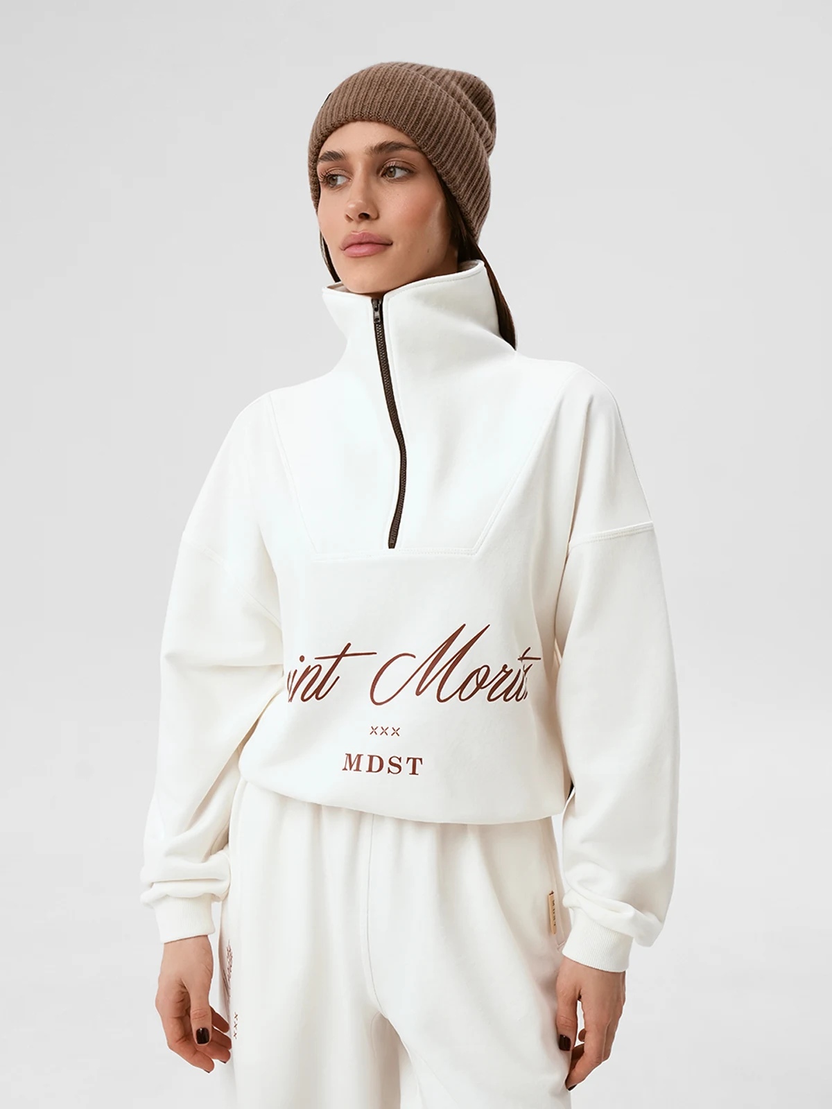 Модель в молочном спортивном костюме SUIT NEVE от MOODSTORIES свободного кроя с вышивкой и шапкой.