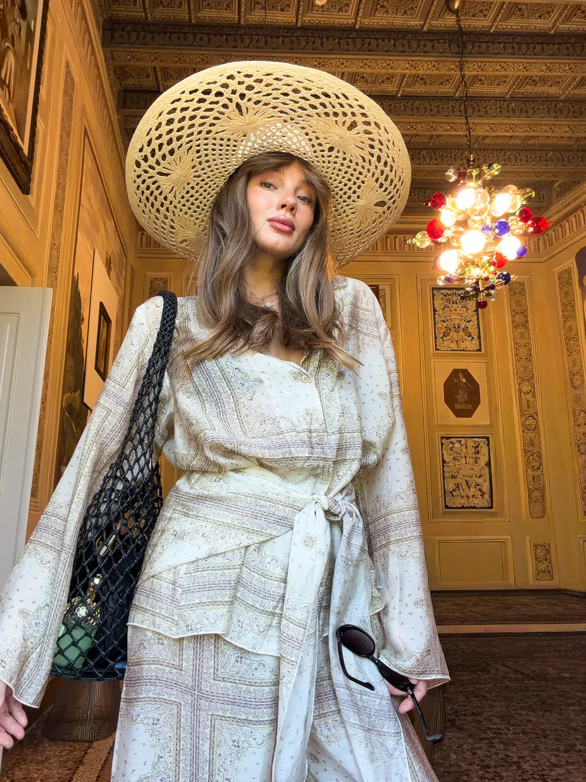 Модель у світлому костюмі-трійці Suit Le Pyjama від MOODSTORIES: вільний жакет, широкі штани та бікіні на тлі басейну.