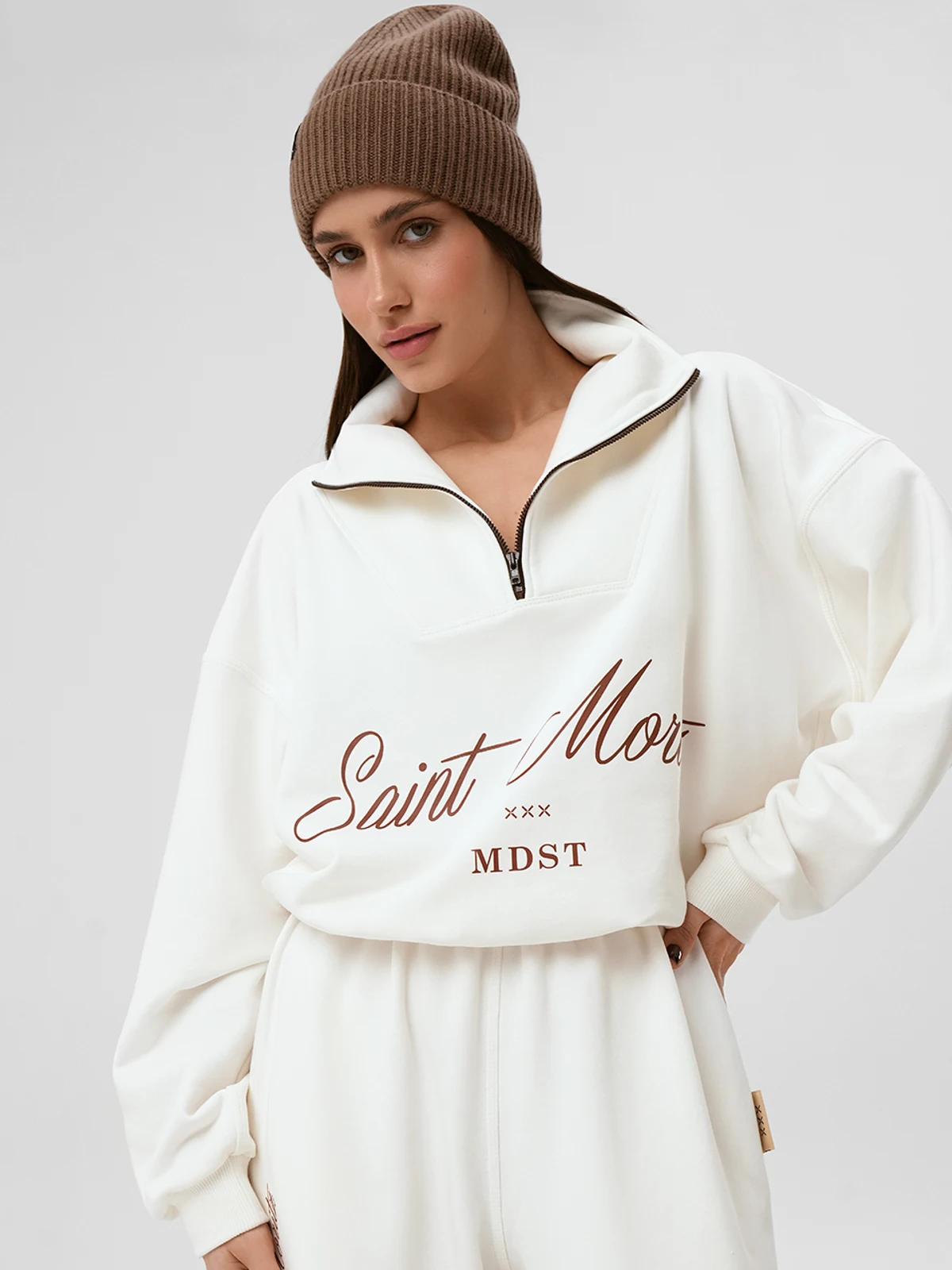 Модель в молочном спортивном костюме SUIT NEVE от MOODSTORIES свободного кроя с вышивкой и шапкой.