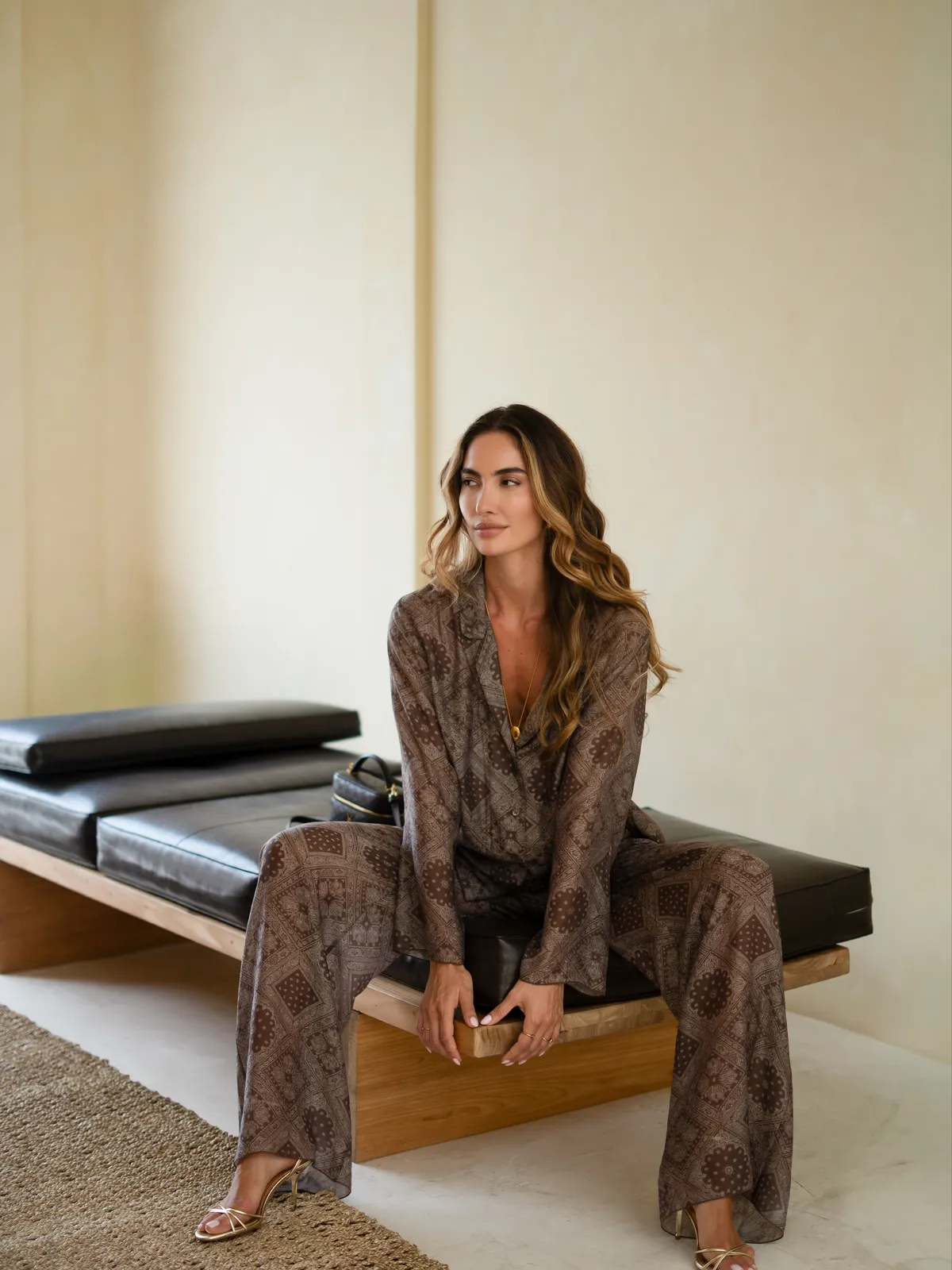 Модель у коричневому костюмі Suit Le Pyjama Brun MOODSTORIES з візерунком, що складається з вільної сорочки-жакета та широких штанів, стоїть біля дверей.