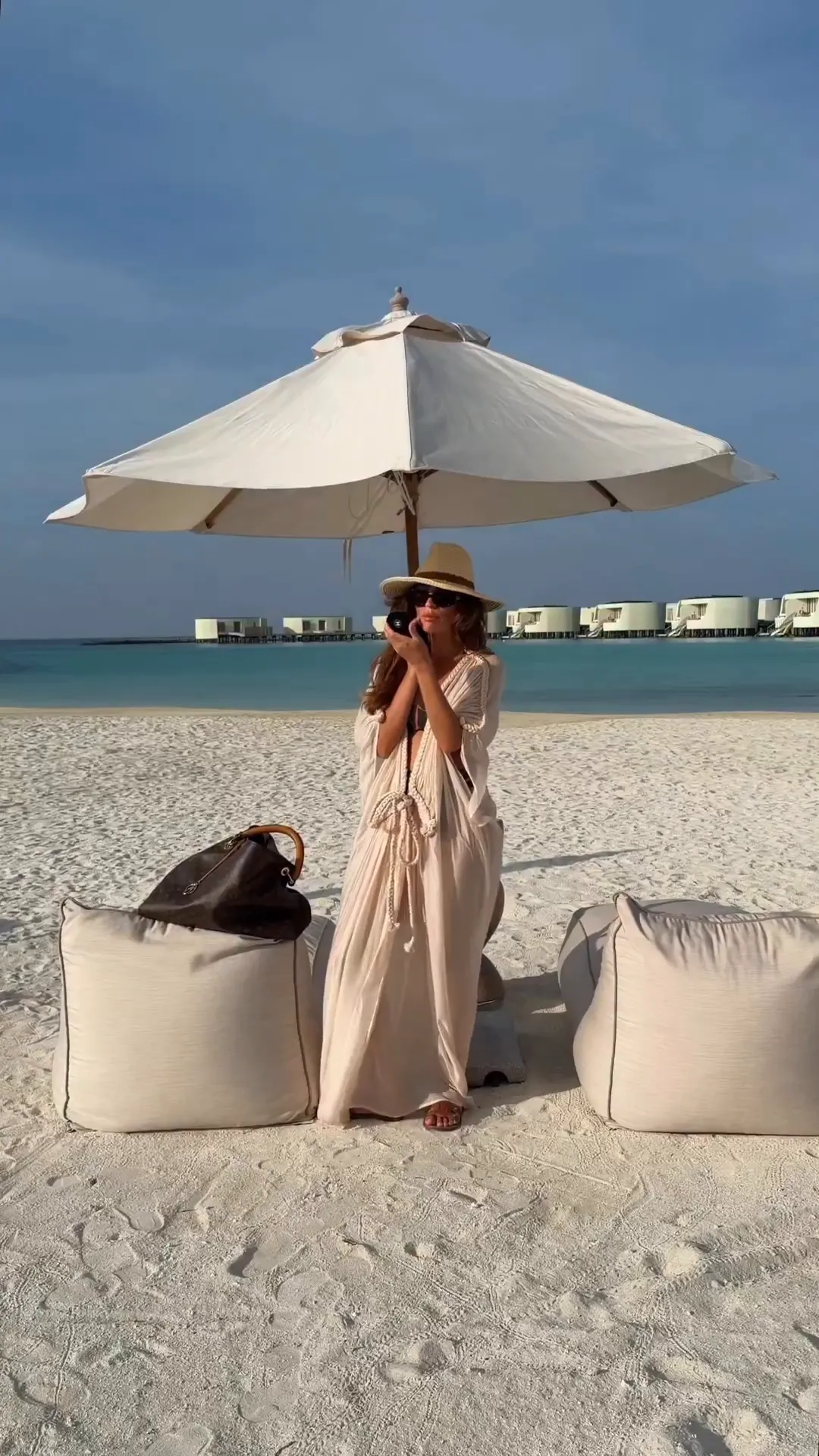 Женщина в длинной тунике Dress Goddress Camel от MOODSTORIES с ручным плетением, держит зонт, стоит среди зелени. – 2