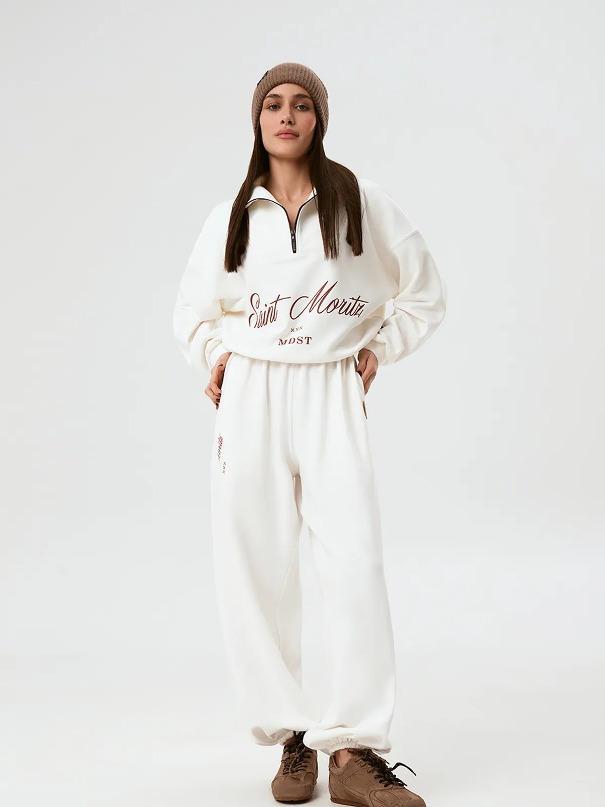 Модель в полный рост, одетая в молочные широкие брюки PANTS NEVE и свитшот, стоит на белом фоне.